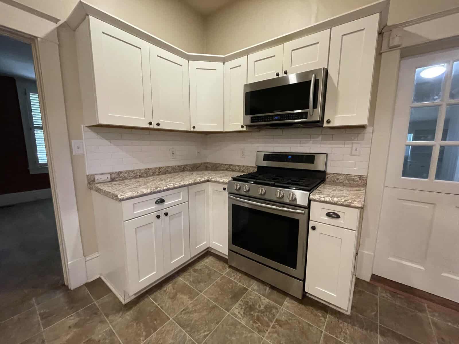 A corner kitchen layout featuring white cabinets, granite countertops, a built-in microwave, and a stainless-steel stove/oven.