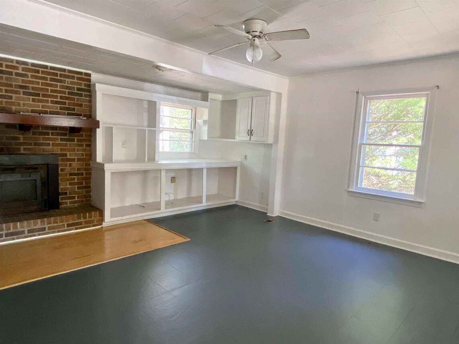 Empty room with a fireplace, built-in shelves, and hardwood floors.
