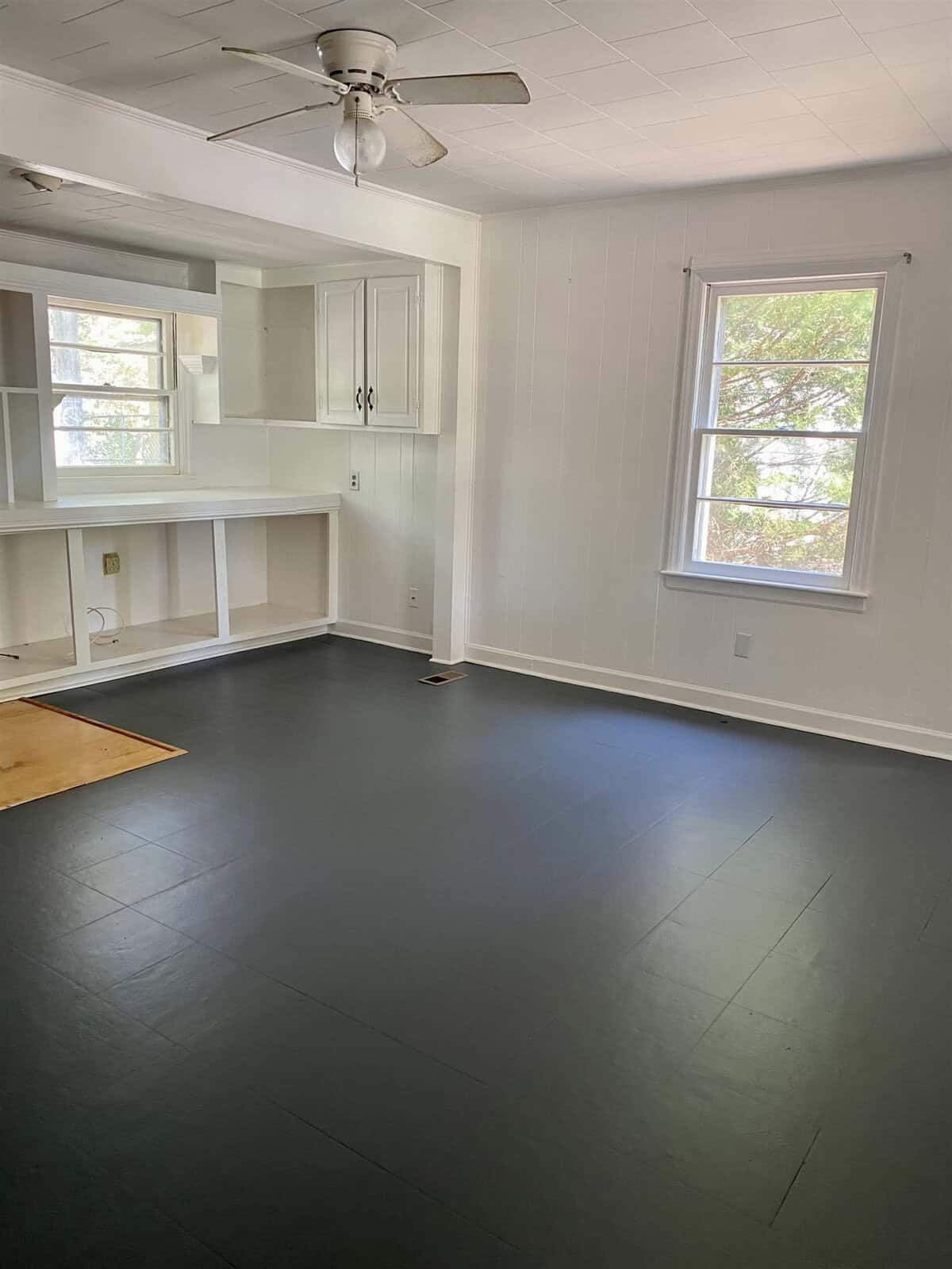 An empty room with white walls, a ceiling fan, built-in shelving, and dark flooring.
