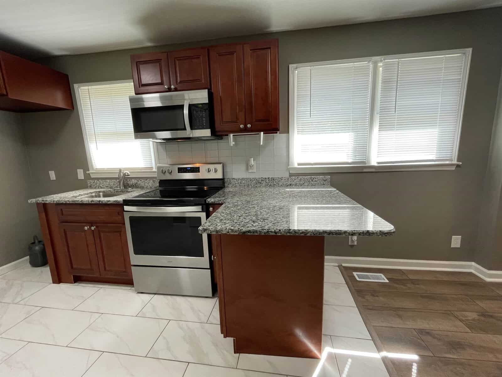 A modern kitchen with stainless steel appliances, dark wood cabinets, and a granite countertop island.