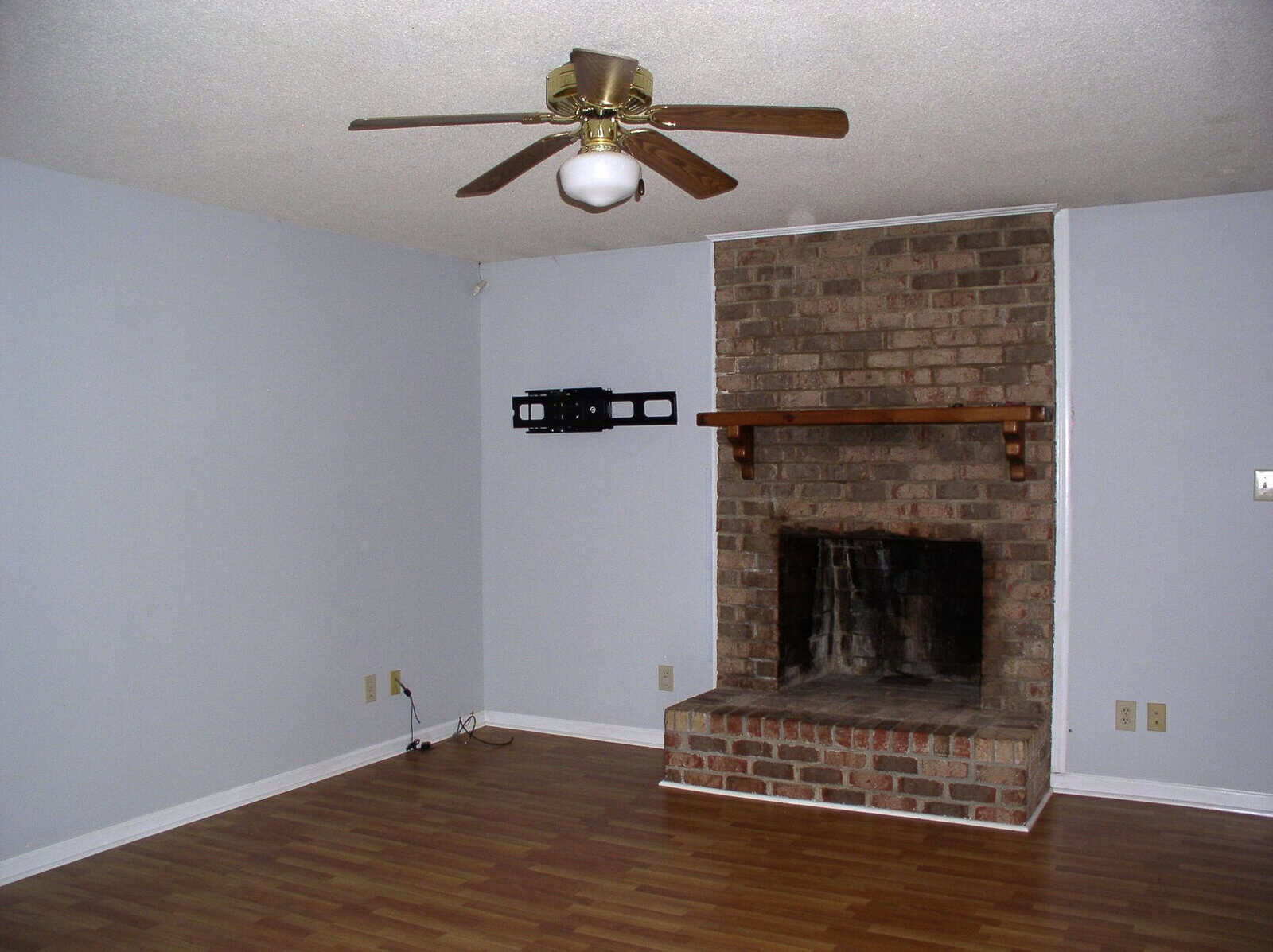 Empty room with a fireplace, hardwood floors, and a ceiling fan.