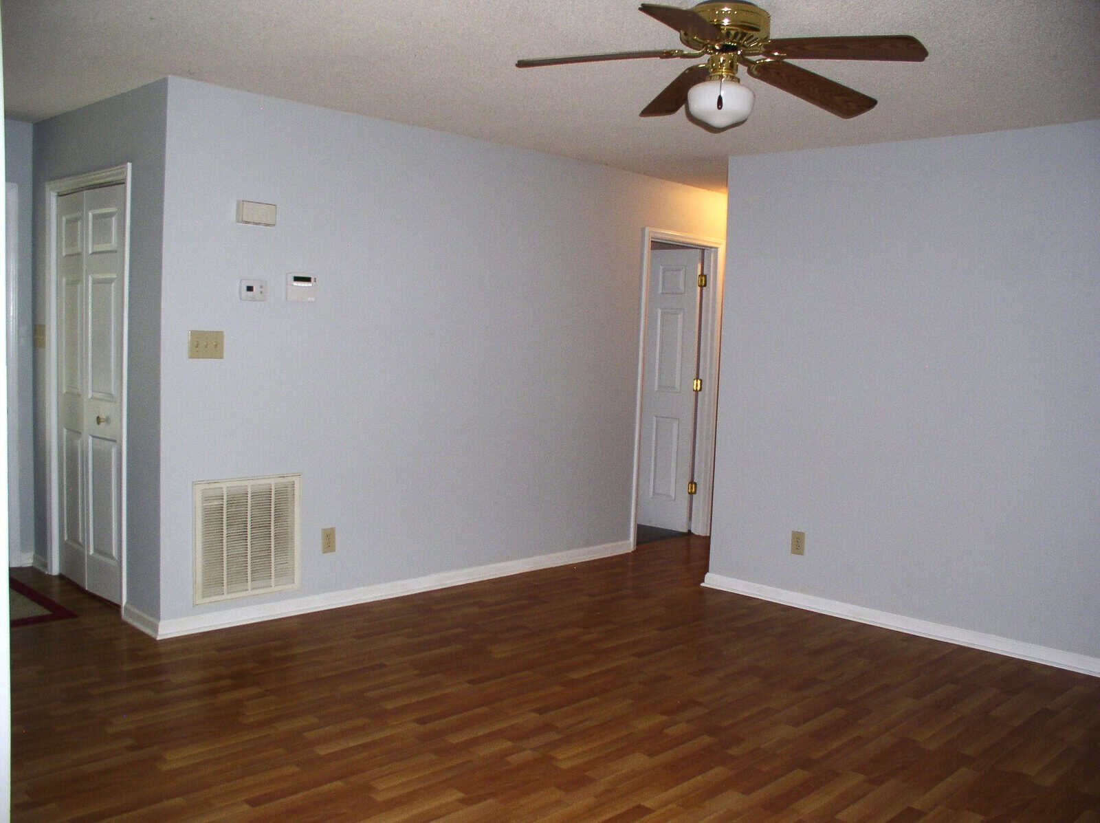 An empty room with hardwood floors, white walls, and a ceiling fan.