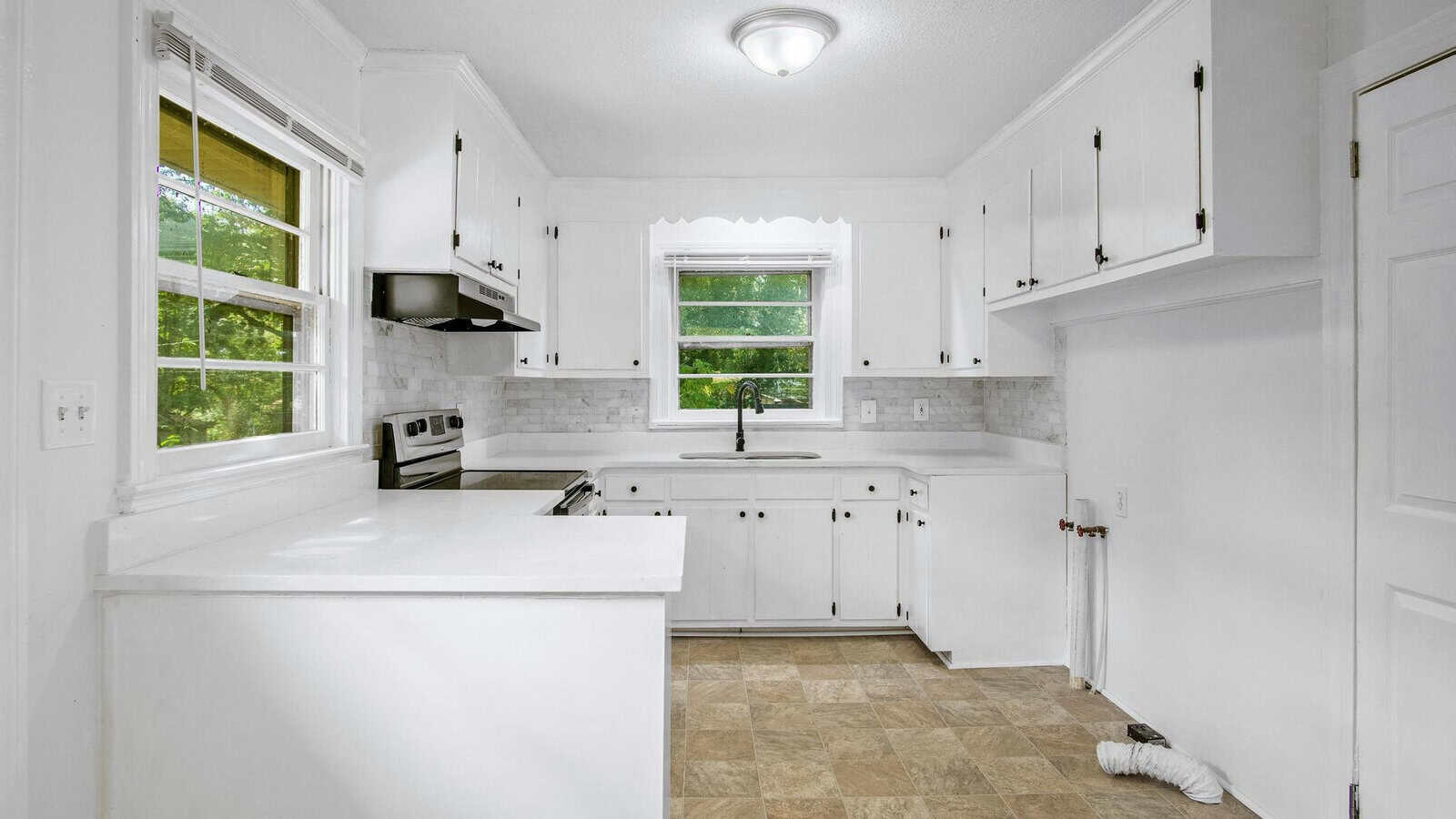 A bright, white-themed kitchen with modern appliances and tiled flooring.