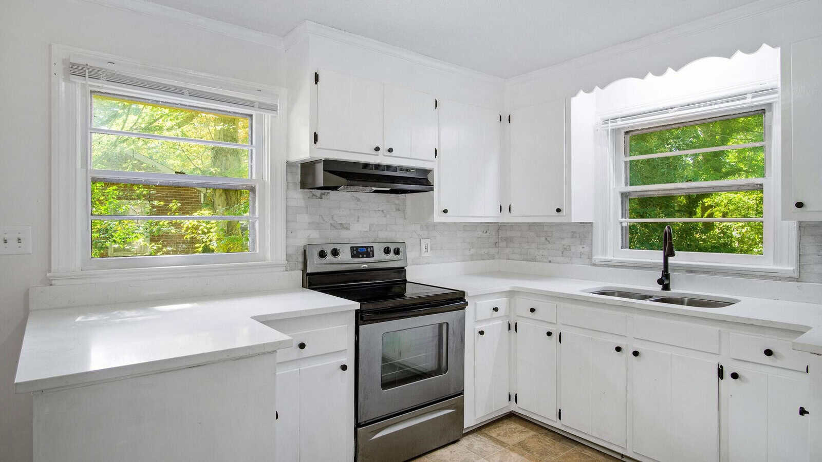 A bright kitchen with white cabinets, stainless steel appliances, and a view of greenery through the windows.