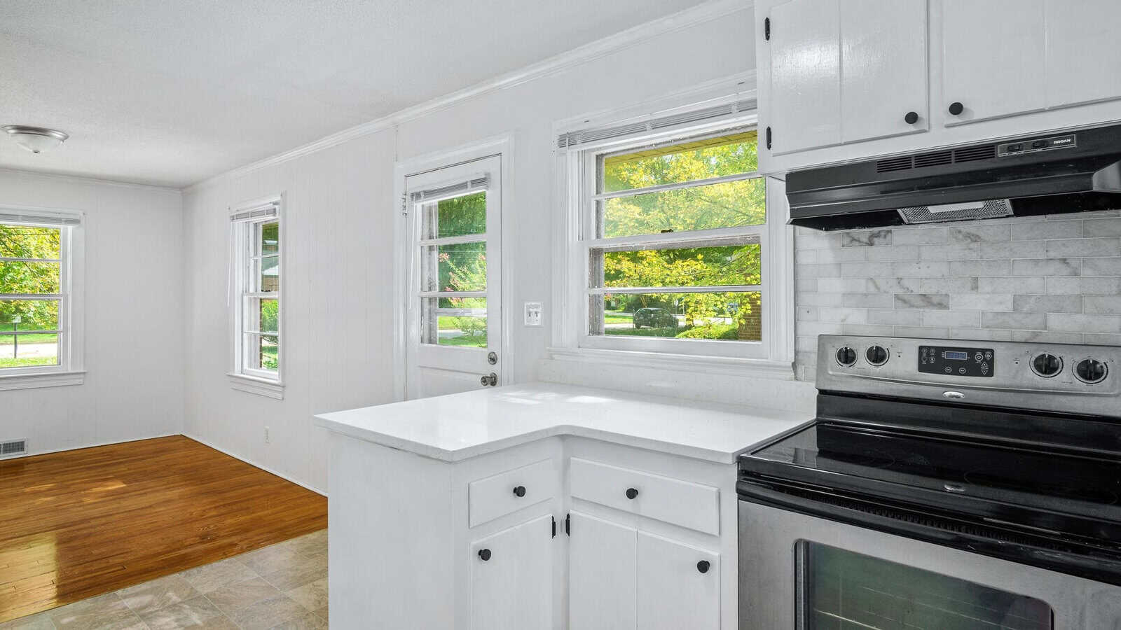 A bright, modern kitchen with white cabinets, stainless steel appliances, and hardwood floors.