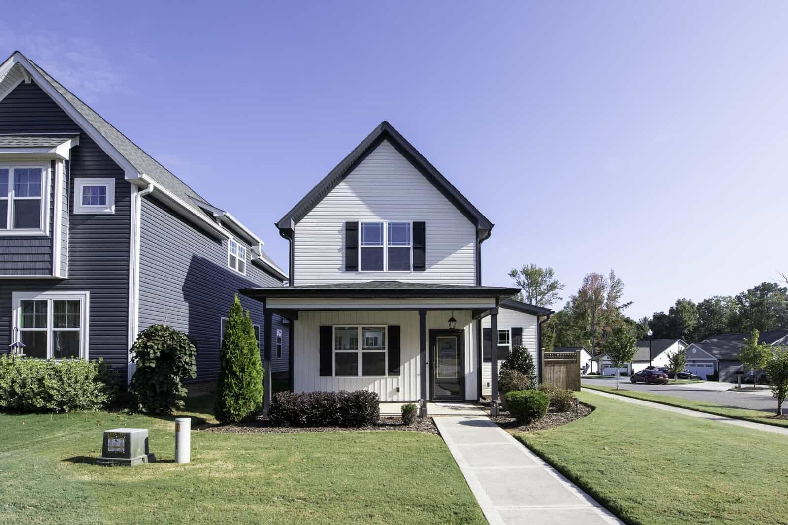 A small, modern two-story house at 115 York Drive features gray siding and a covered front porch, set on a well-maintained green lawn. Surrounded by trees in the charming suburb of Oxford, it basks under a clear blue sky.