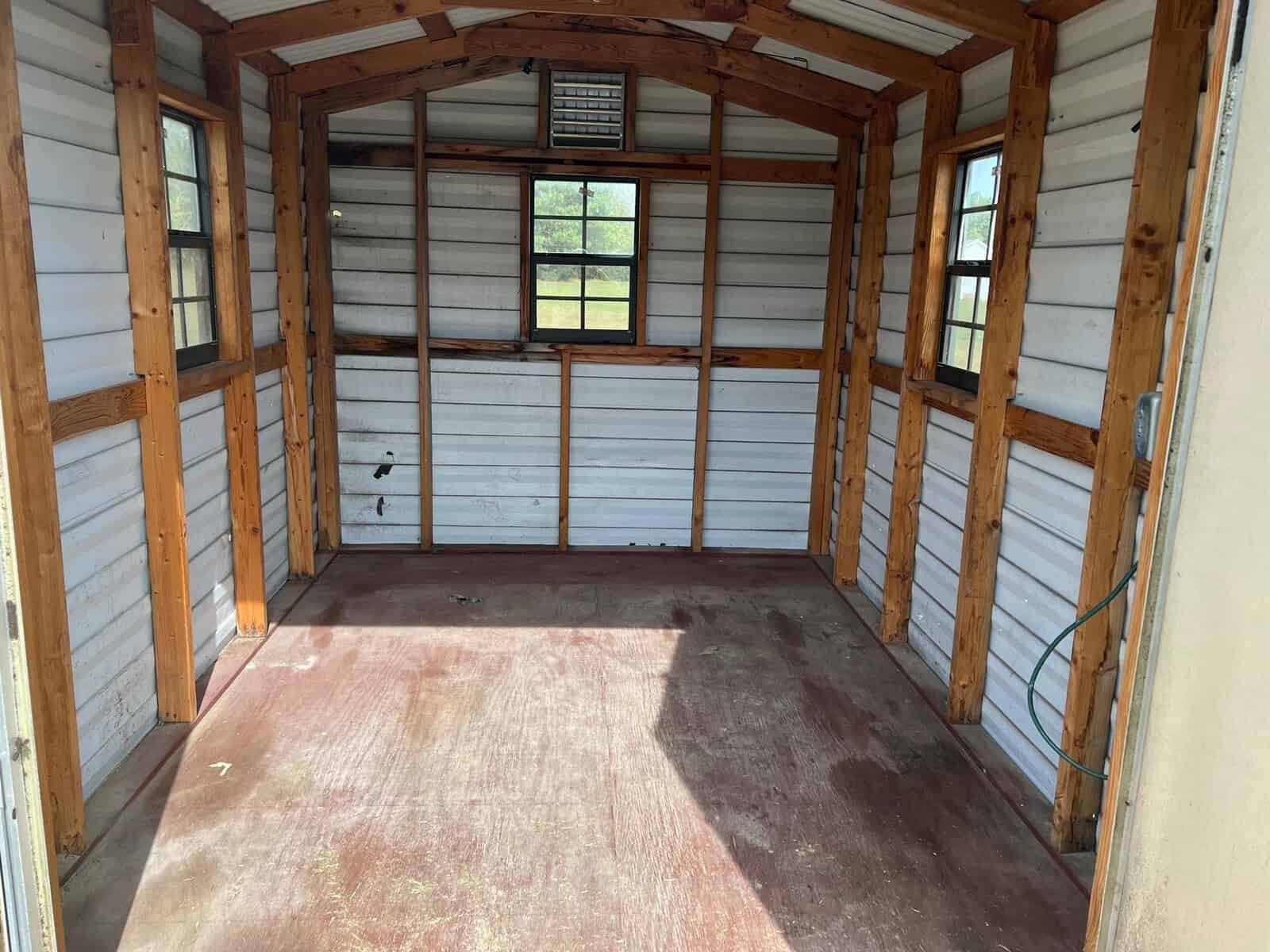 Empty wooden shed interior with open double doors, natural light entering through windows, and a worn floor.
