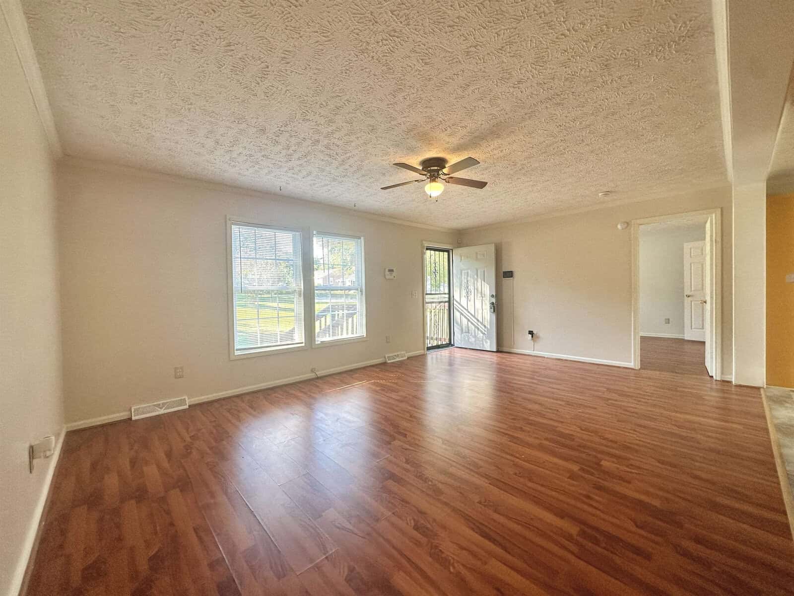 Empty living room with hardwood floors, a ceiling fan, and natural light coming in from windows and a sliding glass door.