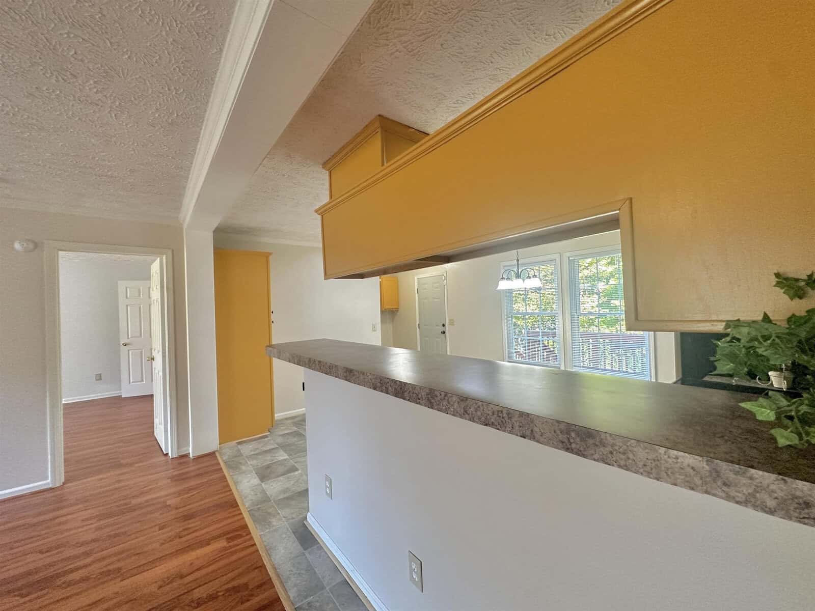 Interior of a house featuring a kitchen with a breakfast bar counter, laminate wood flooring, and a view into adjoining rooms with yellow walls.