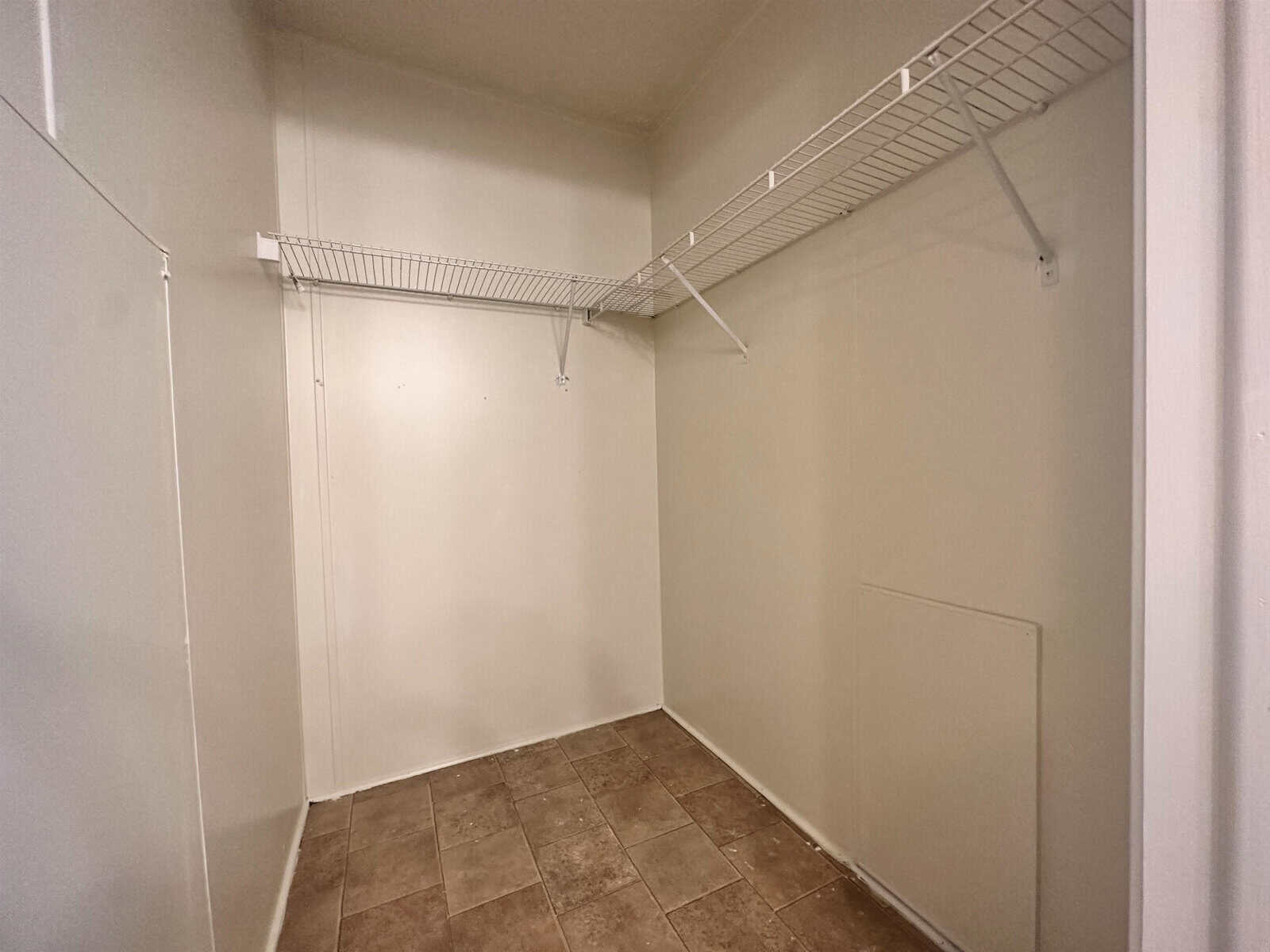 An empty walk-in closet with built-in wire shelving against a bare wall and tiled flooring.