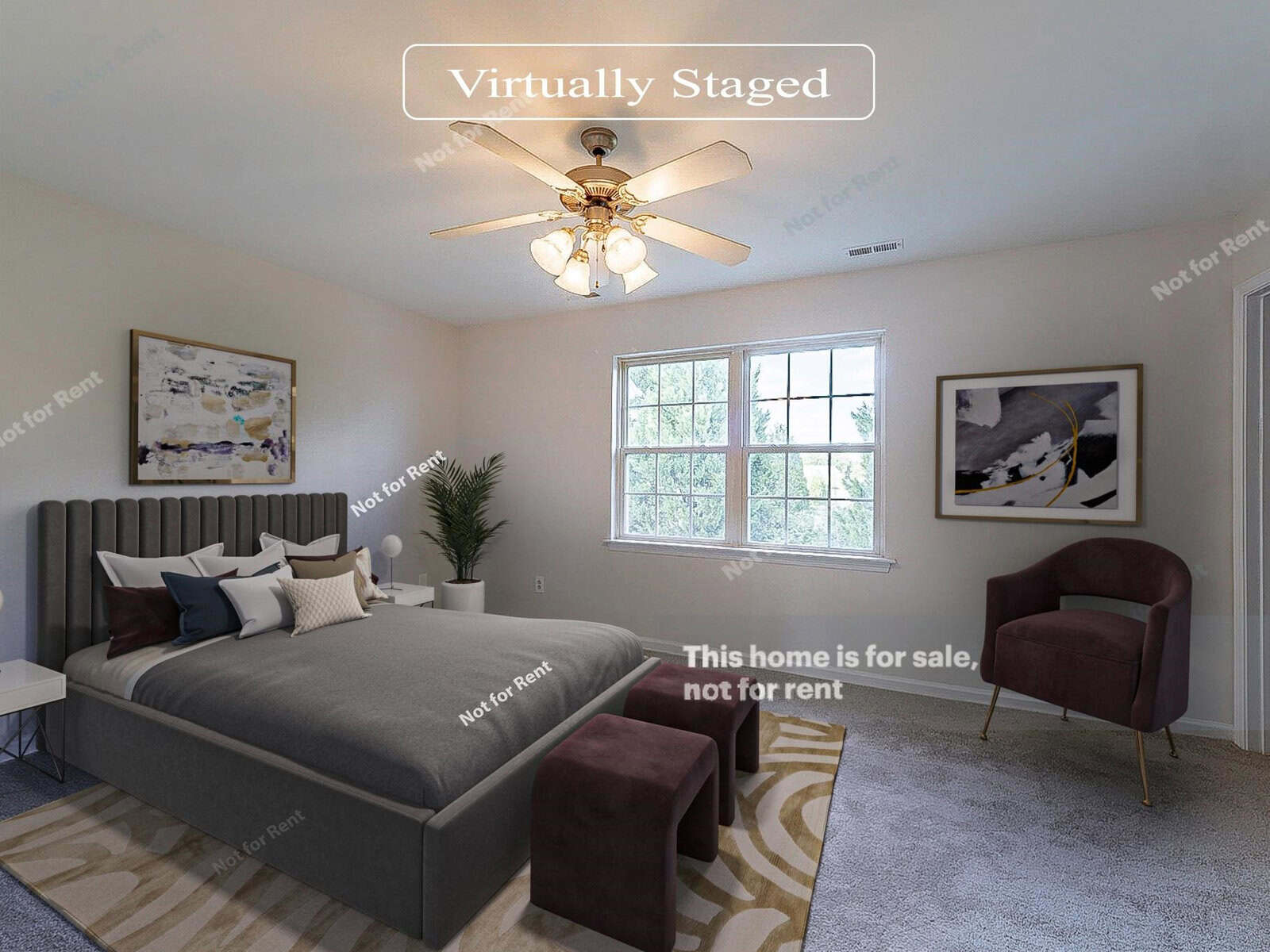 A virtually staged bedroom features a large bed with gray bedding, an upholstered headboard, and matching stools. A ceiling fan hangs above. Abstract art decorates the walls, and a window lets in natural light. A brown chair sits in the corner.
