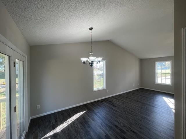 Empty room with gray walls, dark laminate flooring, and a hanging light fixture, featuring a window and an open door leading outside.