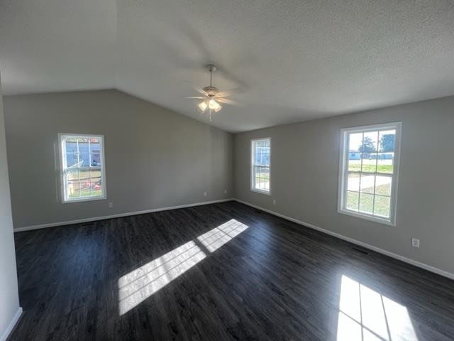 An empty room with grey walls, dark laminate flooring, two windows providing natural light, and a ceiling fan in the center of the room.