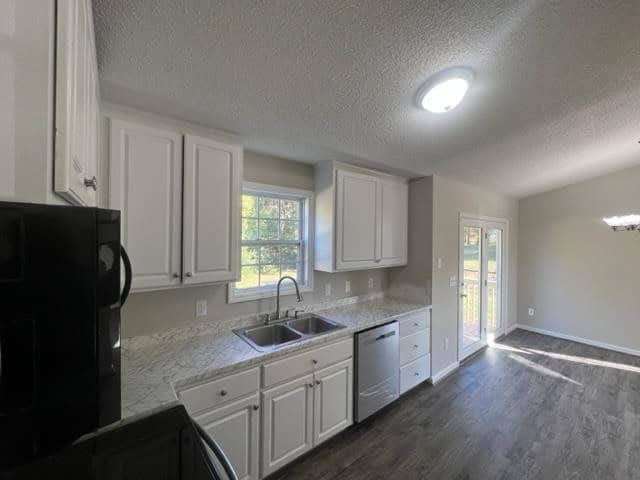 Bright kitchen with white cabinets, granite countertops, modern appliances, and hardwood flooring illuminated by natural light from windows and a central ceiling light.