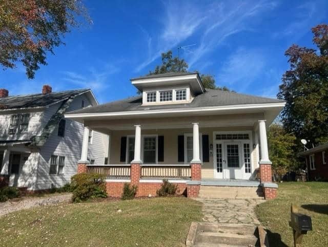 A traditional one-story American house at 116 Zollicoffer Avenue, Henderson NC, with a gray roof and white pillars on the porch. The home is surrounded by grass and trees with autumn foliage