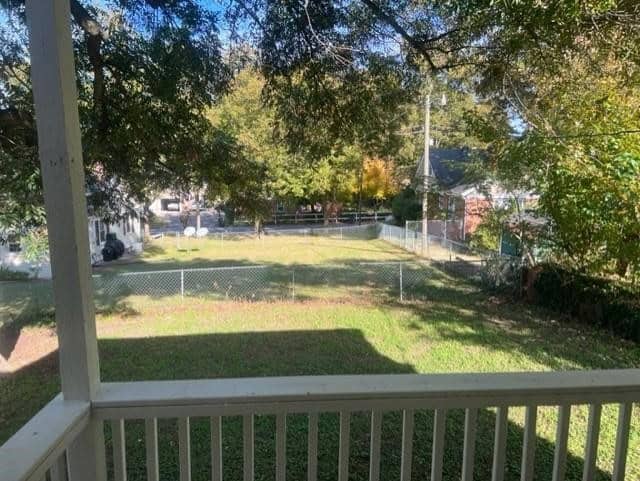 View from a porch showing a fenced lawn, scattered trees with autumn foliage, and neighboring houses in a suburban setting. bright sunlight enhances the scene.