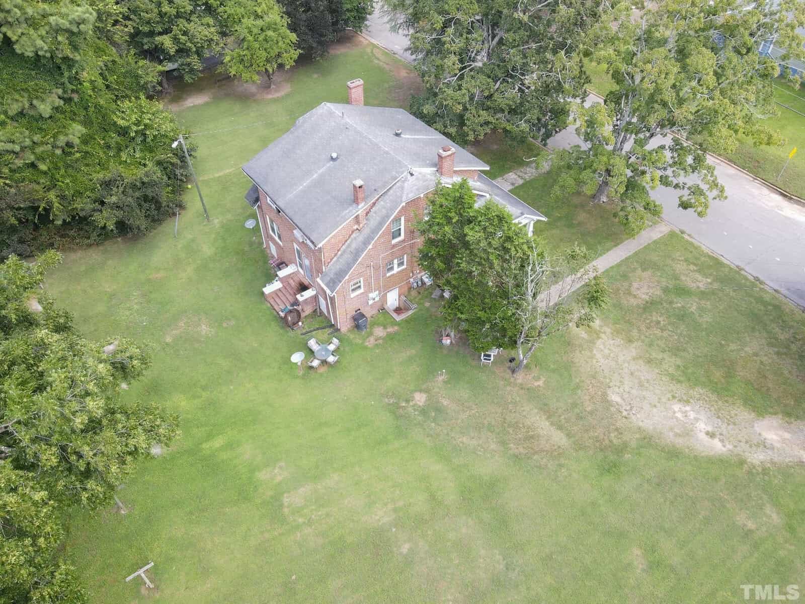 Aerial view of a two-story red brick building surrounded by a green lawn with tables and chairs set up outside, near a pathway and trees.