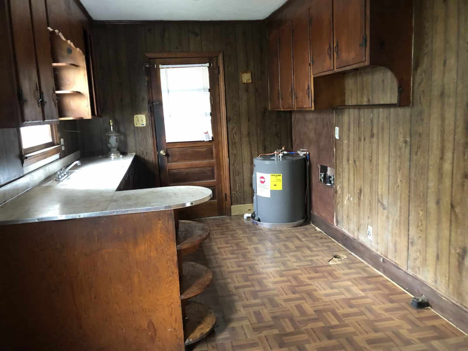 An empty kitchen with wooden paneling, a curved countertop, and a water heater placed on the floor.