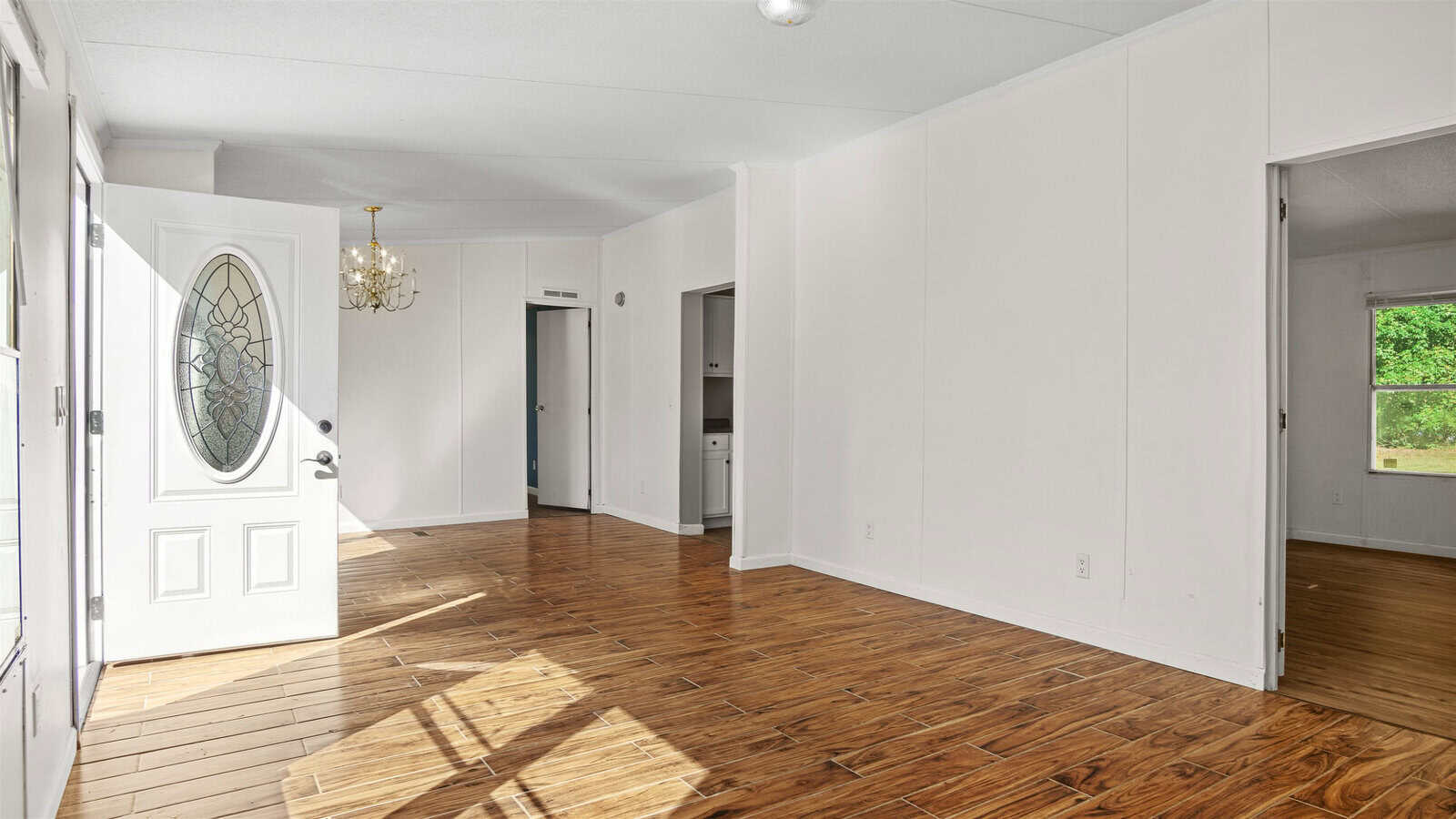 An empty room with herringbone-patterned wooden flooring, white walls, and a white front door featuring a stained-glass window.
