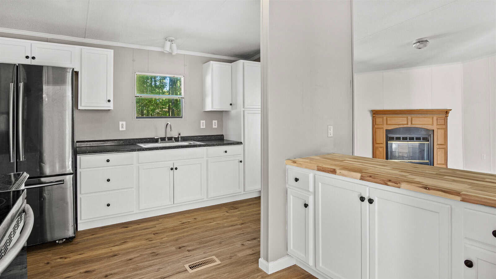 A clean, modern kitchen with white cabinetry, black appliances, and a wooden countertop. the room is well-lit with natural light coming from a window above the sink.