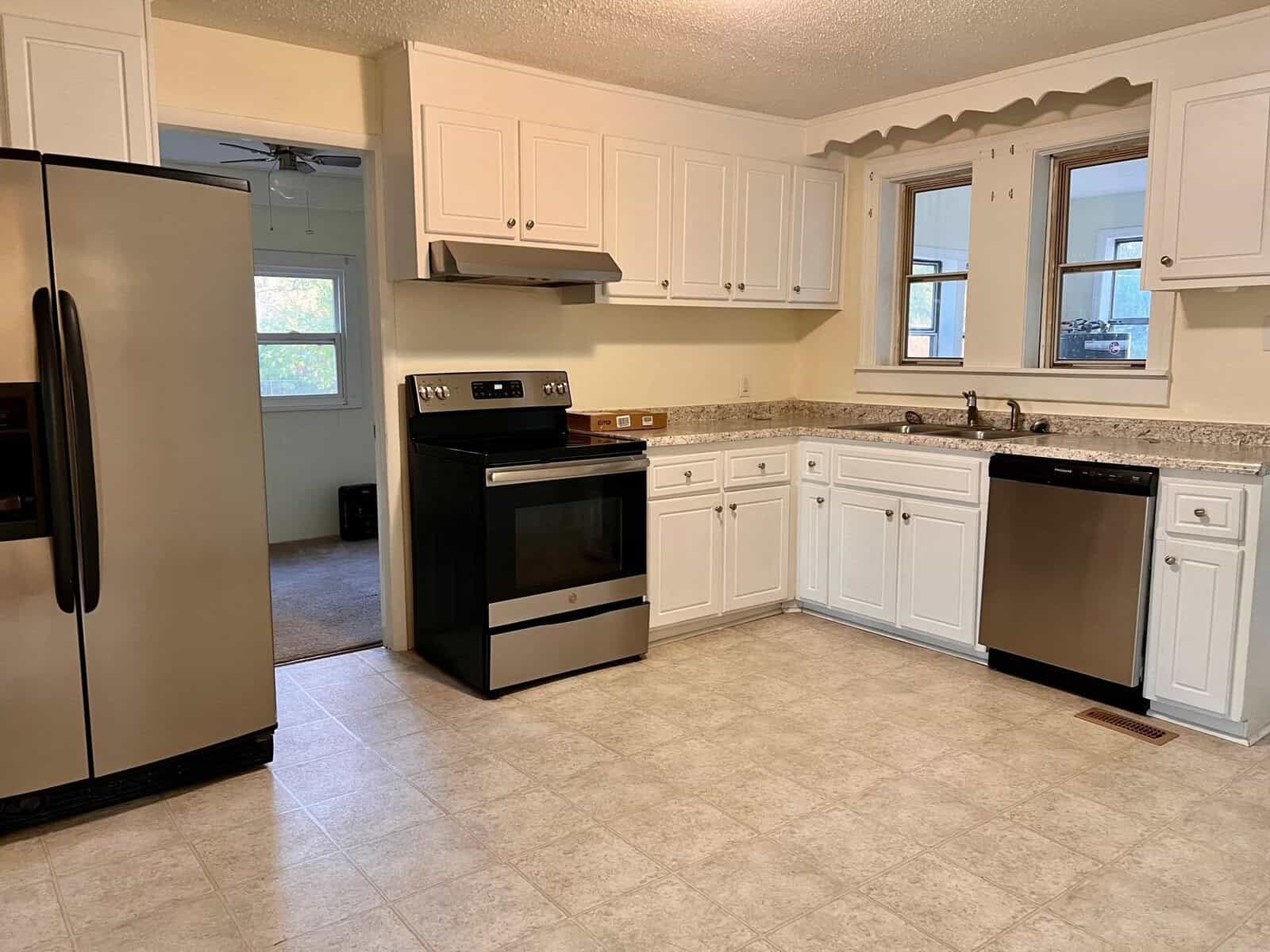 A clean, well-lit kitchen interior featuring white cabinetry, stainless steel appliances, and a tiled floor.