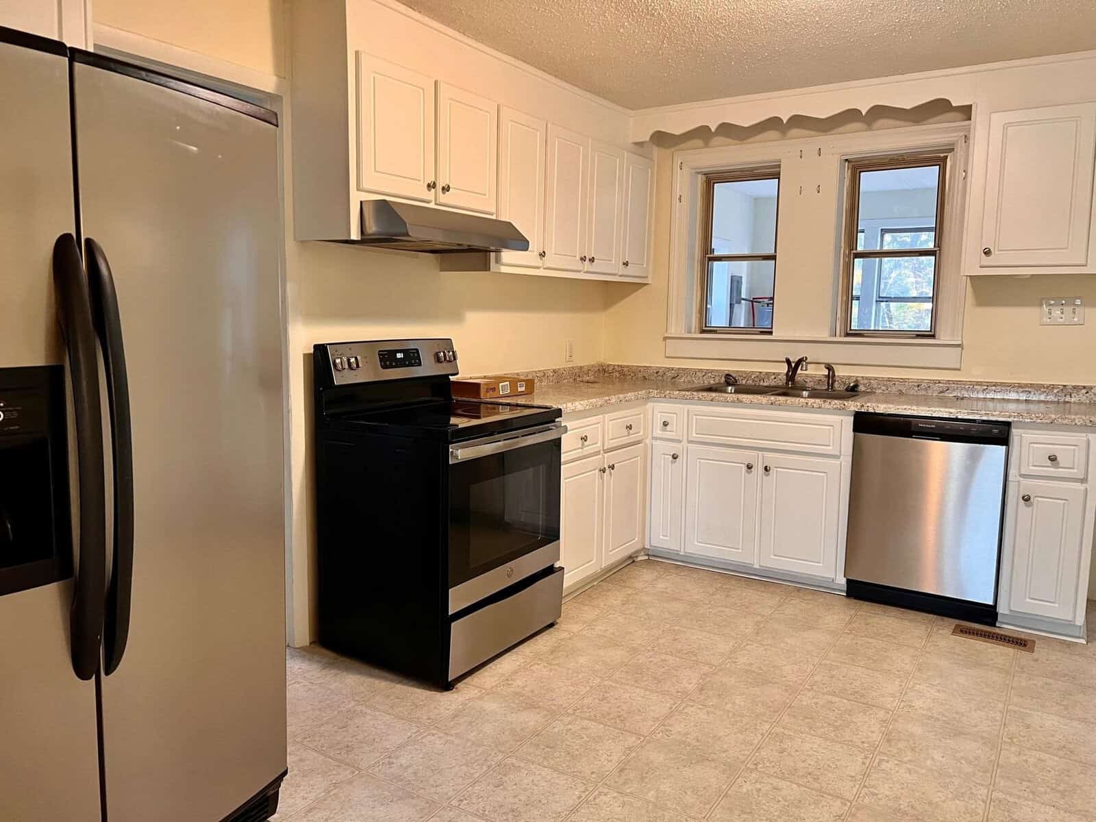 A clean, well-lit kitchen with white cabinetry, granite countertops, and black appliances, including a refrigerator, oven, and dishwasher.