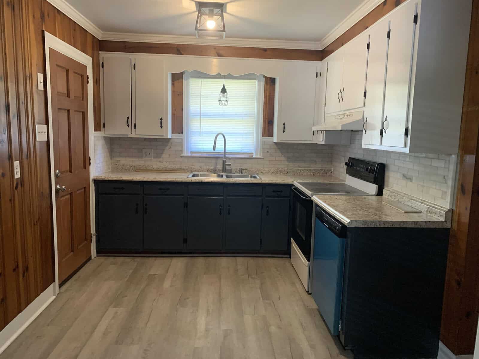 A modern kitchen with white walls, dark blue cabinets, stainless steel appliances, a subway tile backsplash, and wood flooring.