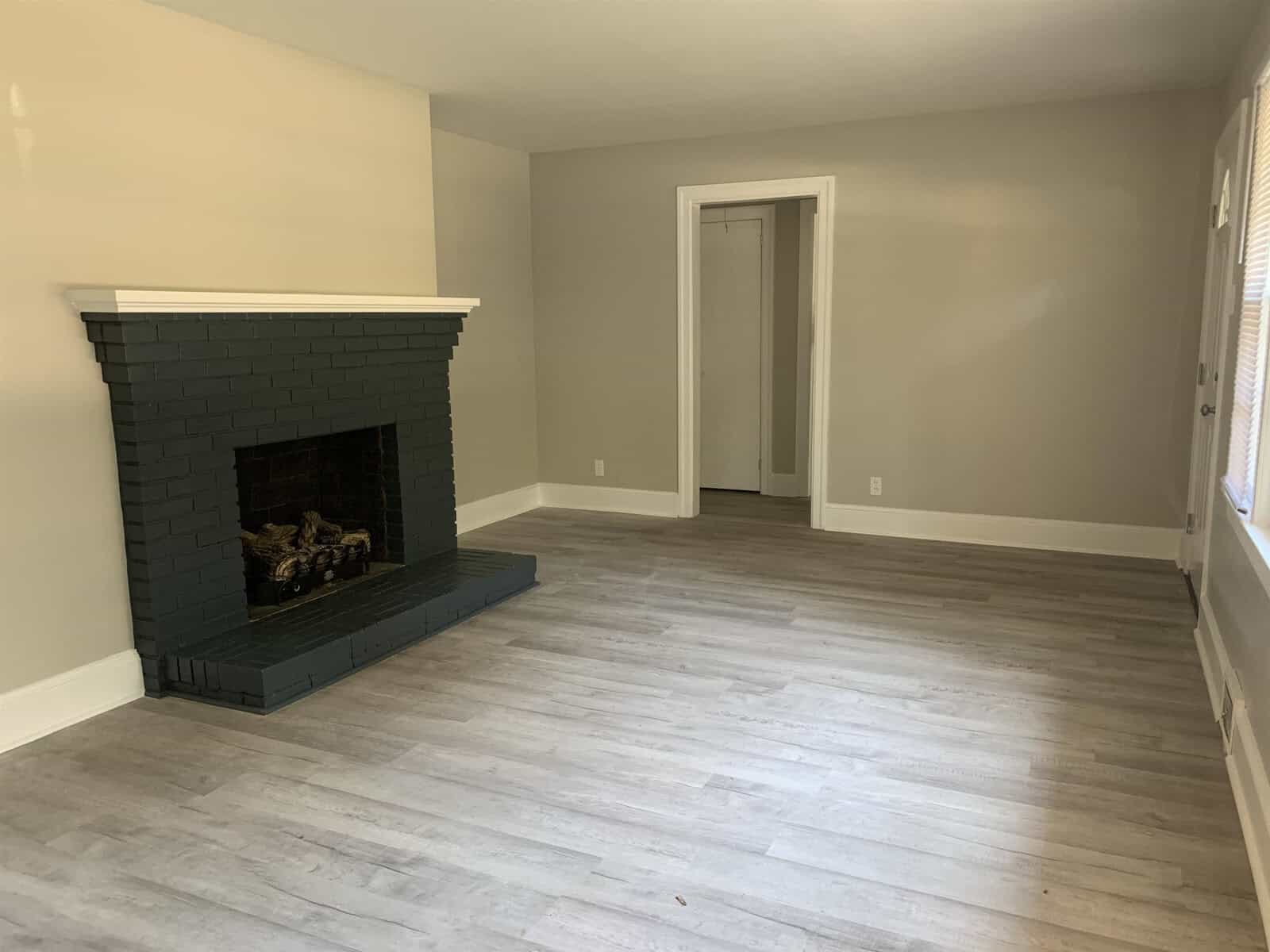 A vacant room with laminate flooring, white walls, and a dark green-tiled fireplace.