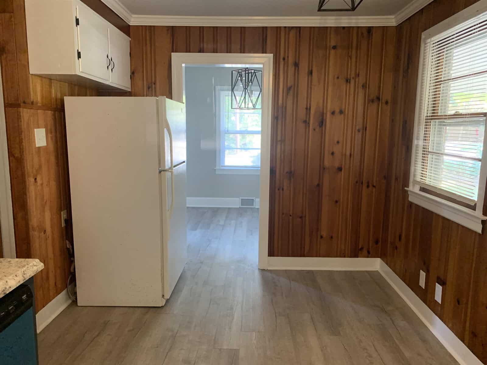 A kitchen with wood-paneled walls, a white refrigerator, and a doorway leading to an adjacent room.