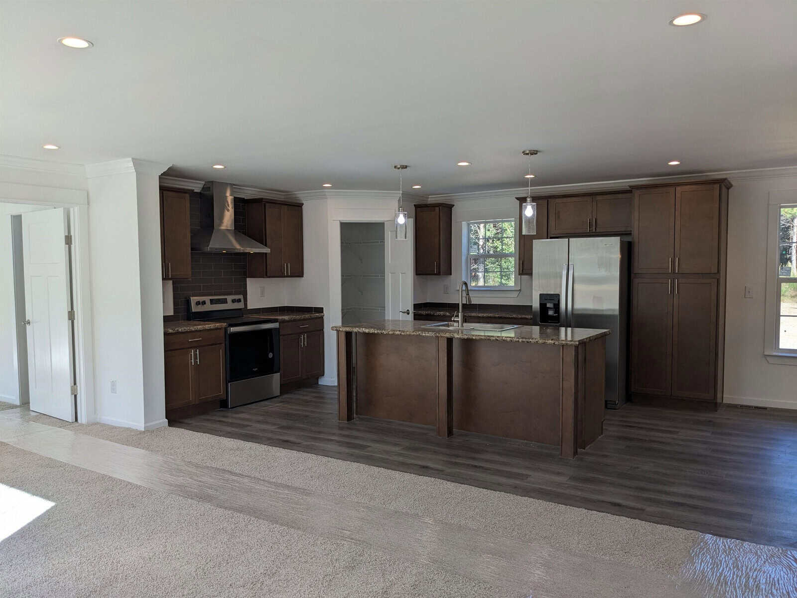 A modern kitchen with stainless steel appliances, an island, and dark wood cabinetry, adjacent to a room with a carpeted floor.