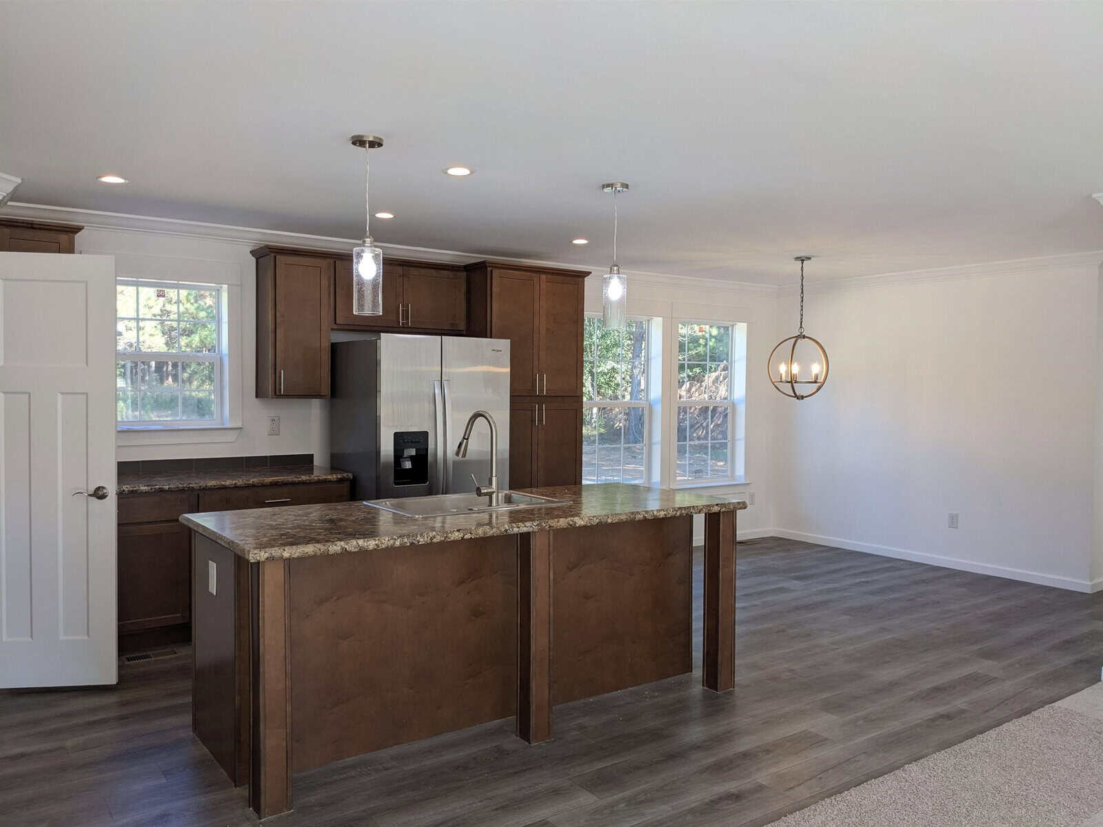 Modern kitchen interior with wooden cabinets, stainless steel appliances, an island with a sink, and pendant lighting.