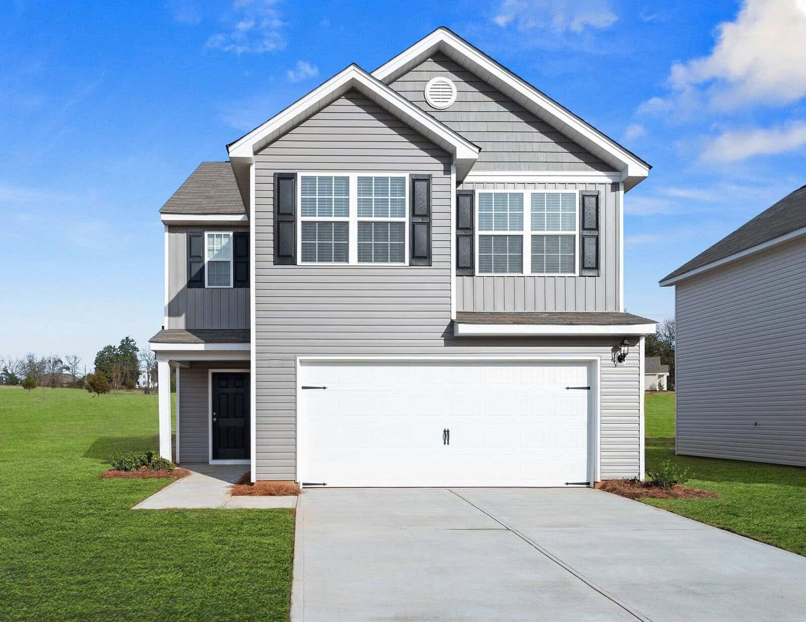 A two-story gray house with white trim and a double garage sits gracefully on 109 Hybrid Street in Oxford. It features a well-maintained lawn and a sidewalk leading to the entrance, while the clear blue sky enhances the serene neighborhood setting.