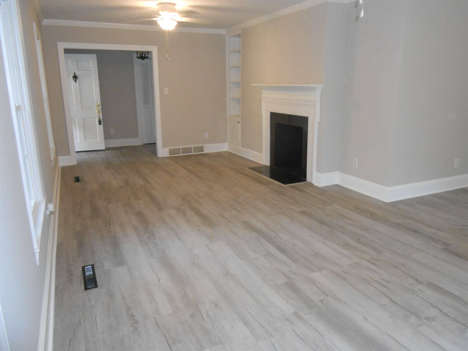 An empty living room with light gray wooden flooring, off-white walls, a black hearth fireplace, and multiple doorways. a measuring device is on the floor.