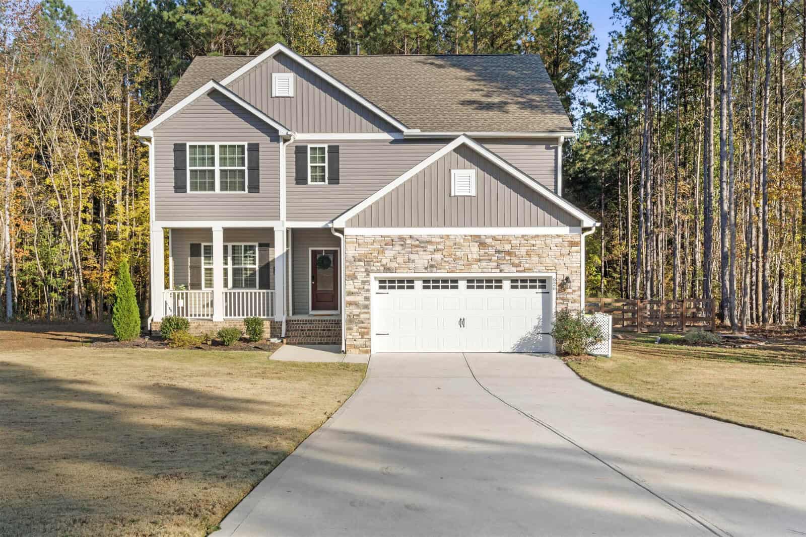 This charming two-story gray and white house on Creedmoor features a stone accent facade and an attached garage, nestled on 926 Weatherby Lane. Surrounded by a lush grassy yard and trees, the well-lit home boasts a welcoming driveway leading to the homey porch.
