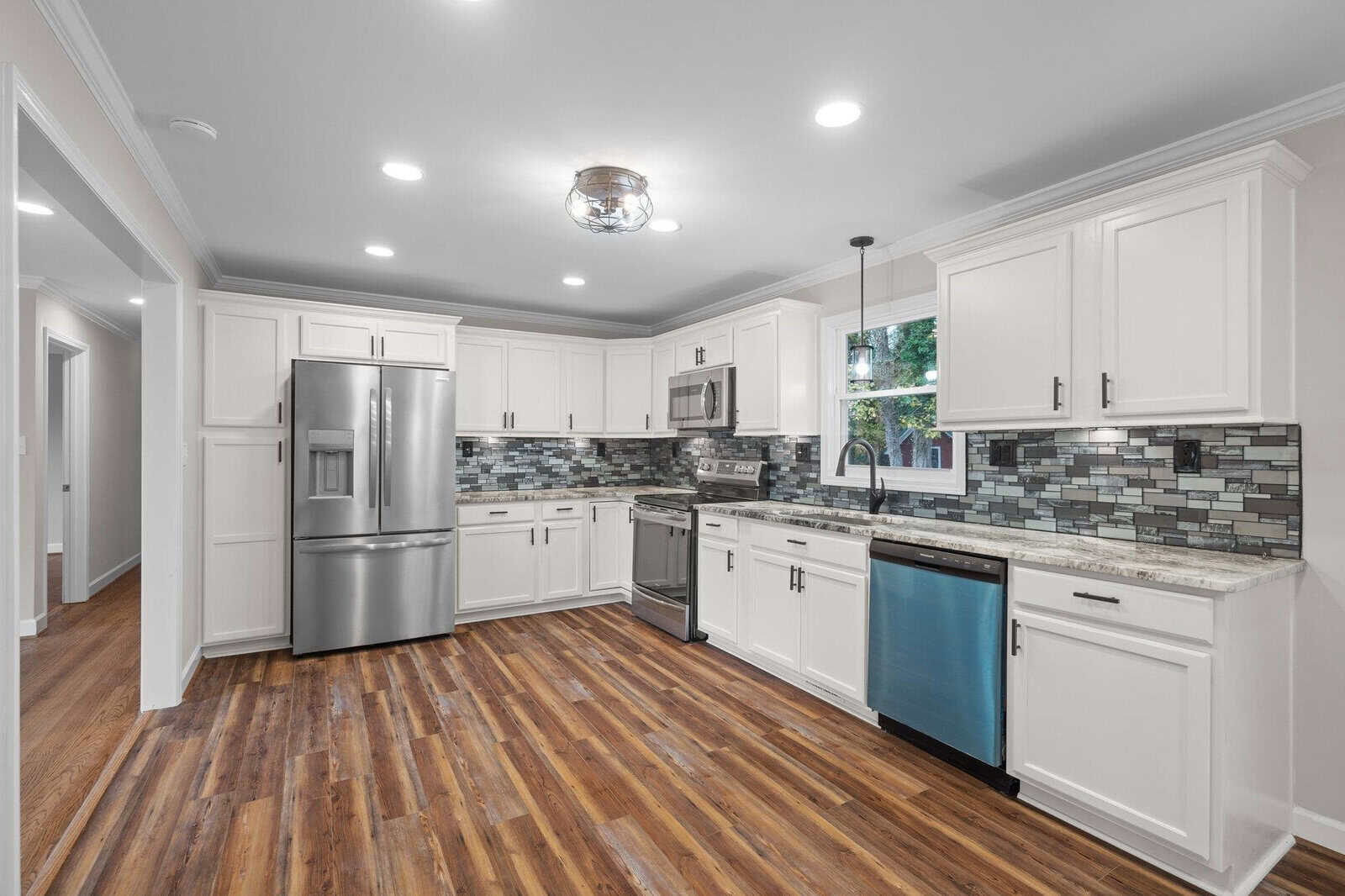 Modern kitchen interior with stainless steel appliances, white cabinetry, and hardwood floors.