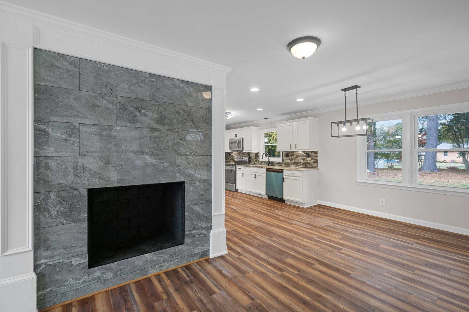 A spacious room featuring polished hardwood floors and a modern fireplace, with an open-plan kitchen visible in the background.