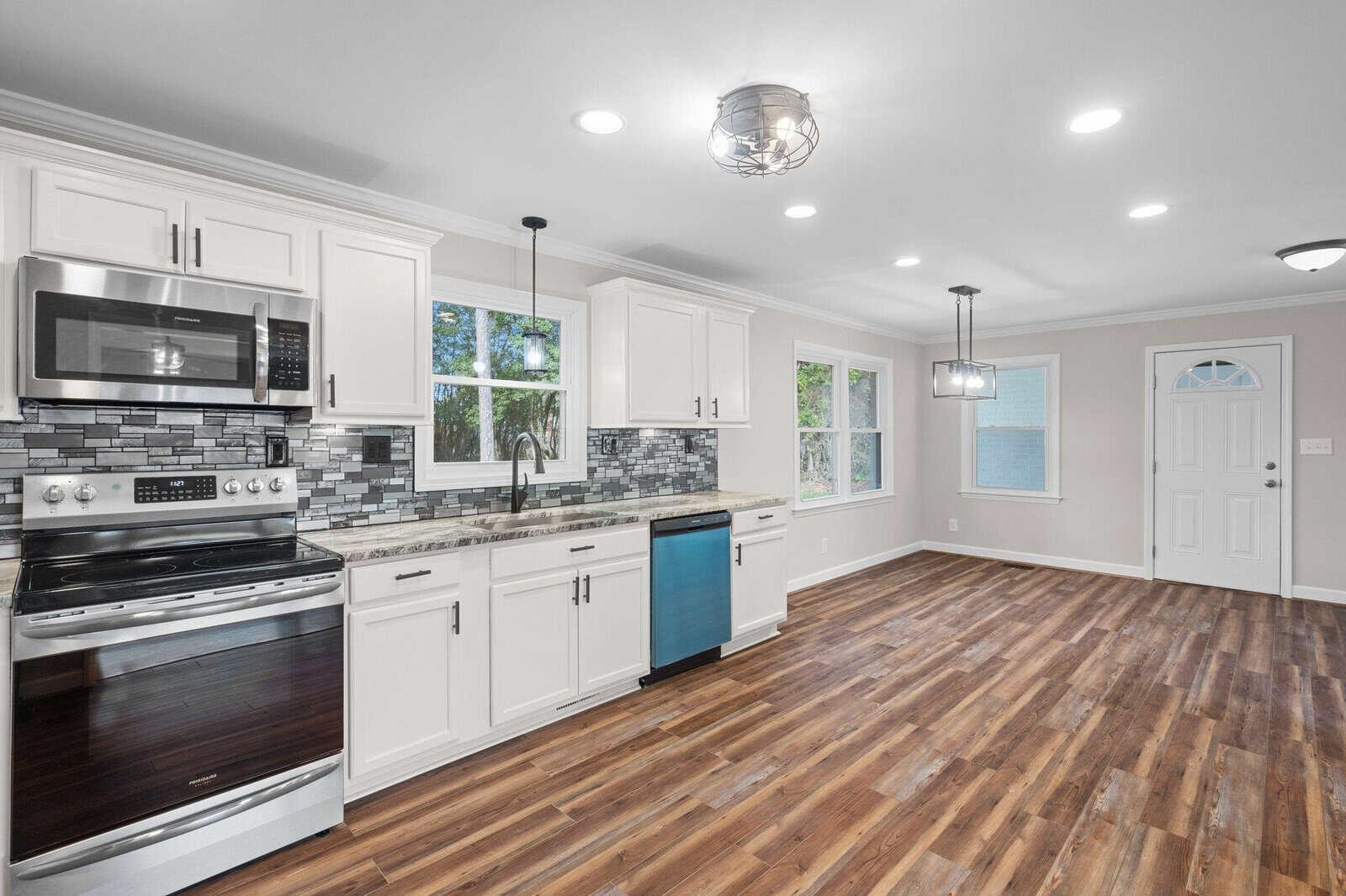 A modern kitchen interior with white cabinetry, stainless steel appliances, hardwood floors, and a blue accent on the lower cabinet of the kitchen island.