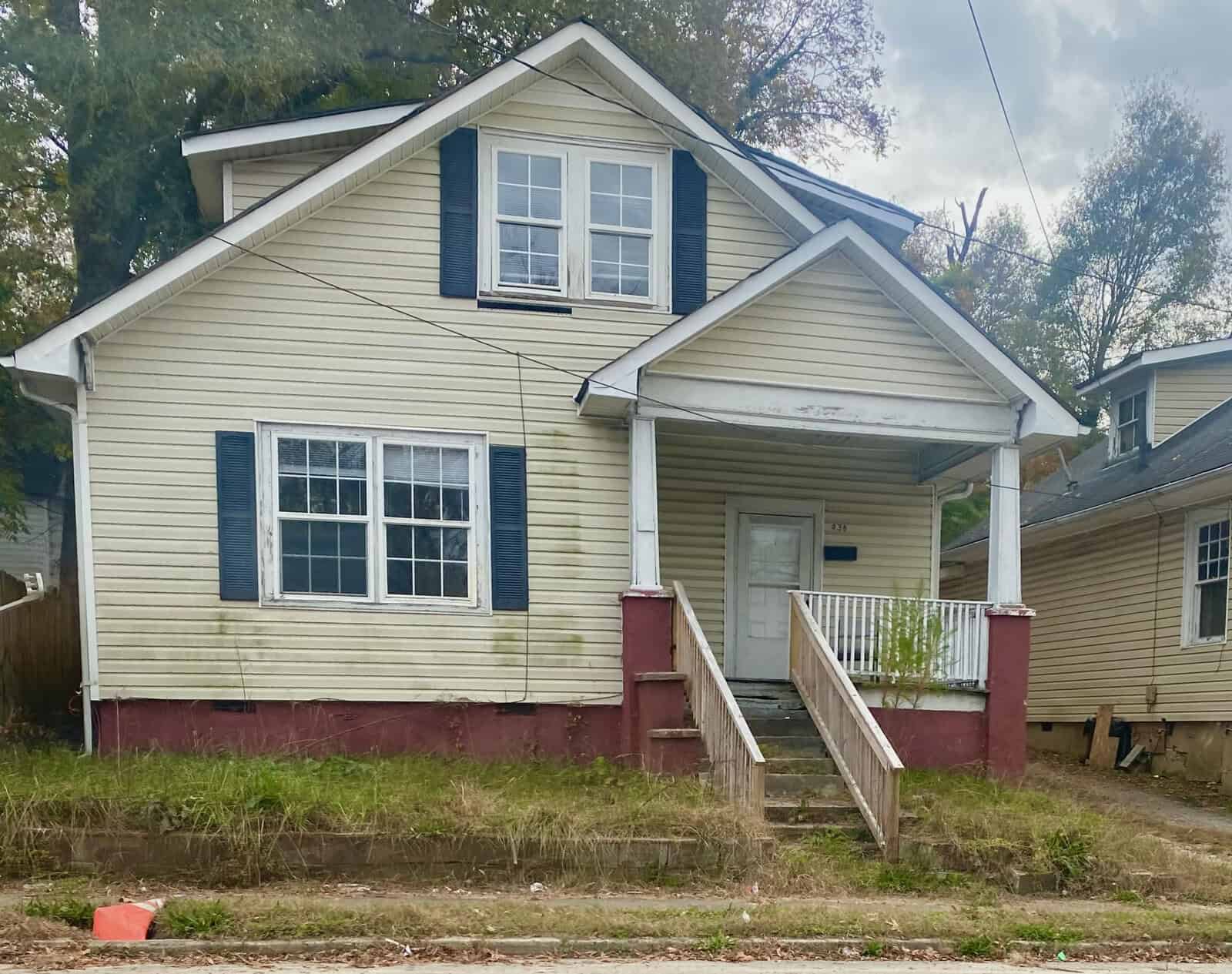 A two-story yellow house with white trim and a front porch in need of maintenance, located at 436 N Chestnut Street, Henderson NC, displays signs of wear and weathering on the exterior.