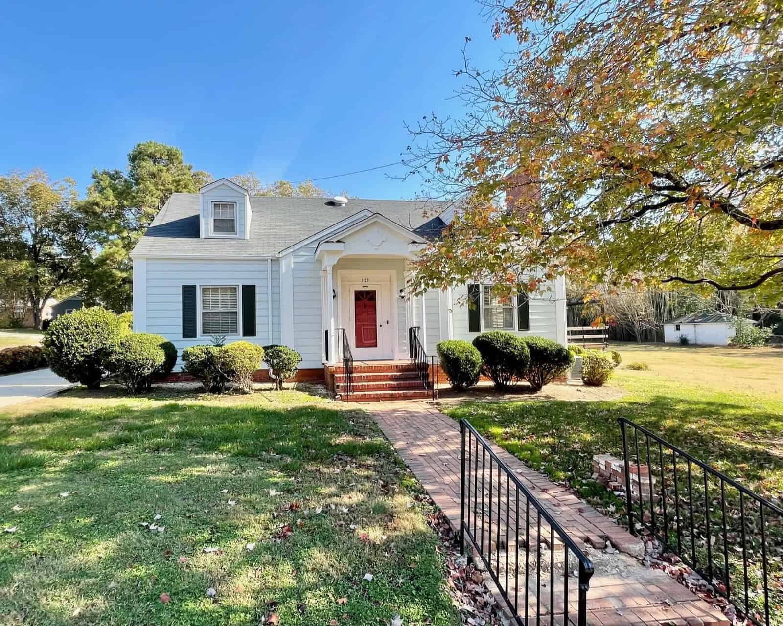 A single-family house at 129 Lakeview Drive, Henderson NC, with white siding and a blue trim, featuring a red front door and a gabled roof, surrounded by a manicured lawn with
