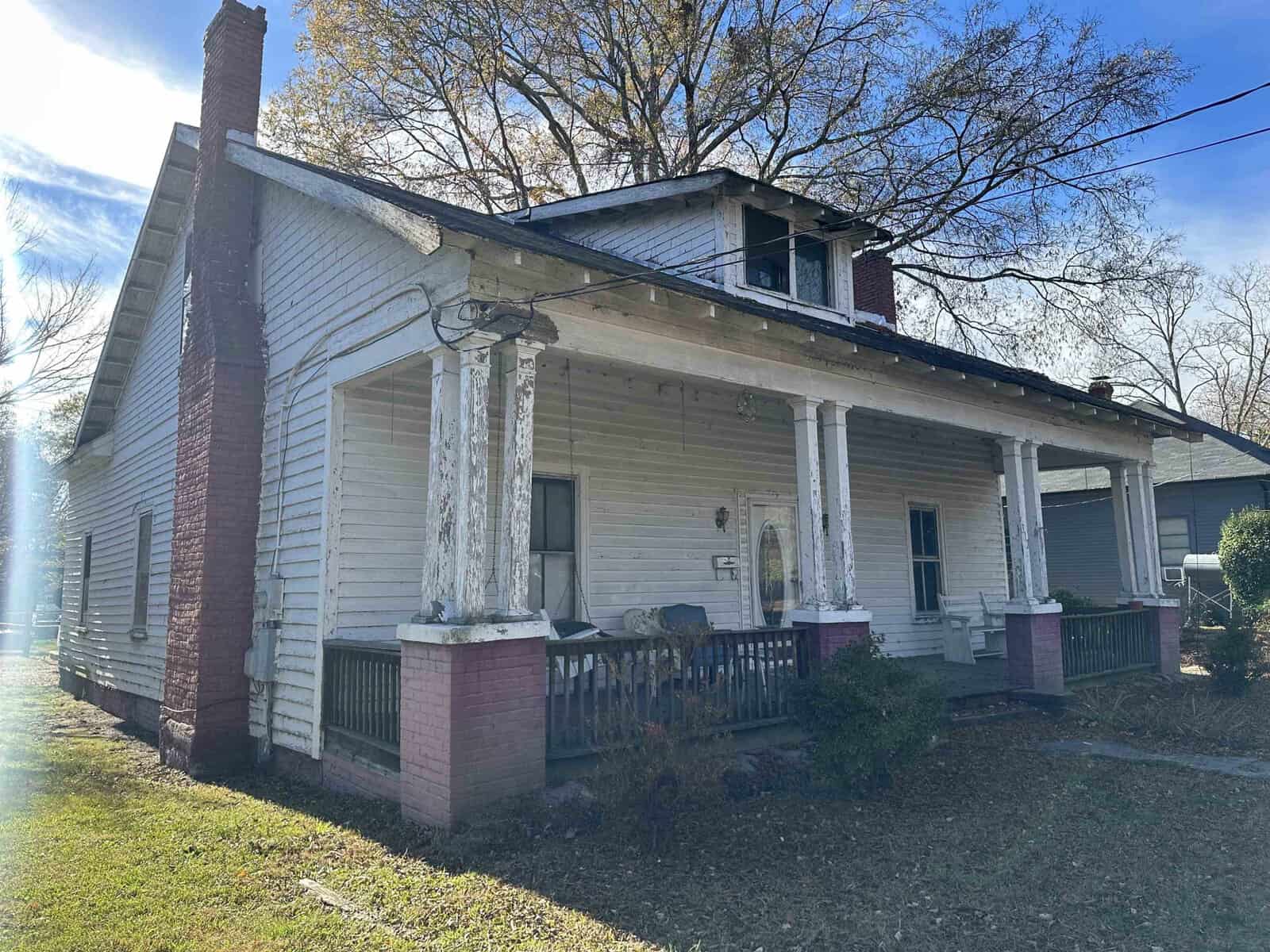 An old, weathered house with peeling paint and a covered porch captured during daylight, with visible signs of disrepair and neglect.