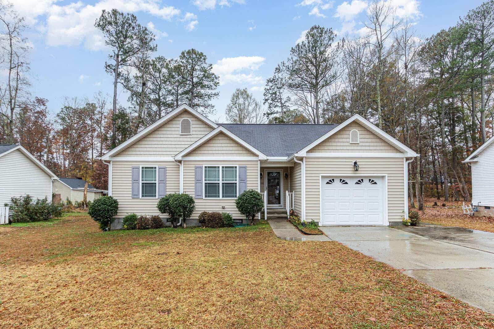 Located at 1198 E Middleton Drive in Creedmoor, this beige single-story house features a gabled roof and an attached garage. A neatly trimmed lawn complements the paved driveway, while a few bushes add charm to the front. Tall trees stand in the background under a partly cloudy sky.