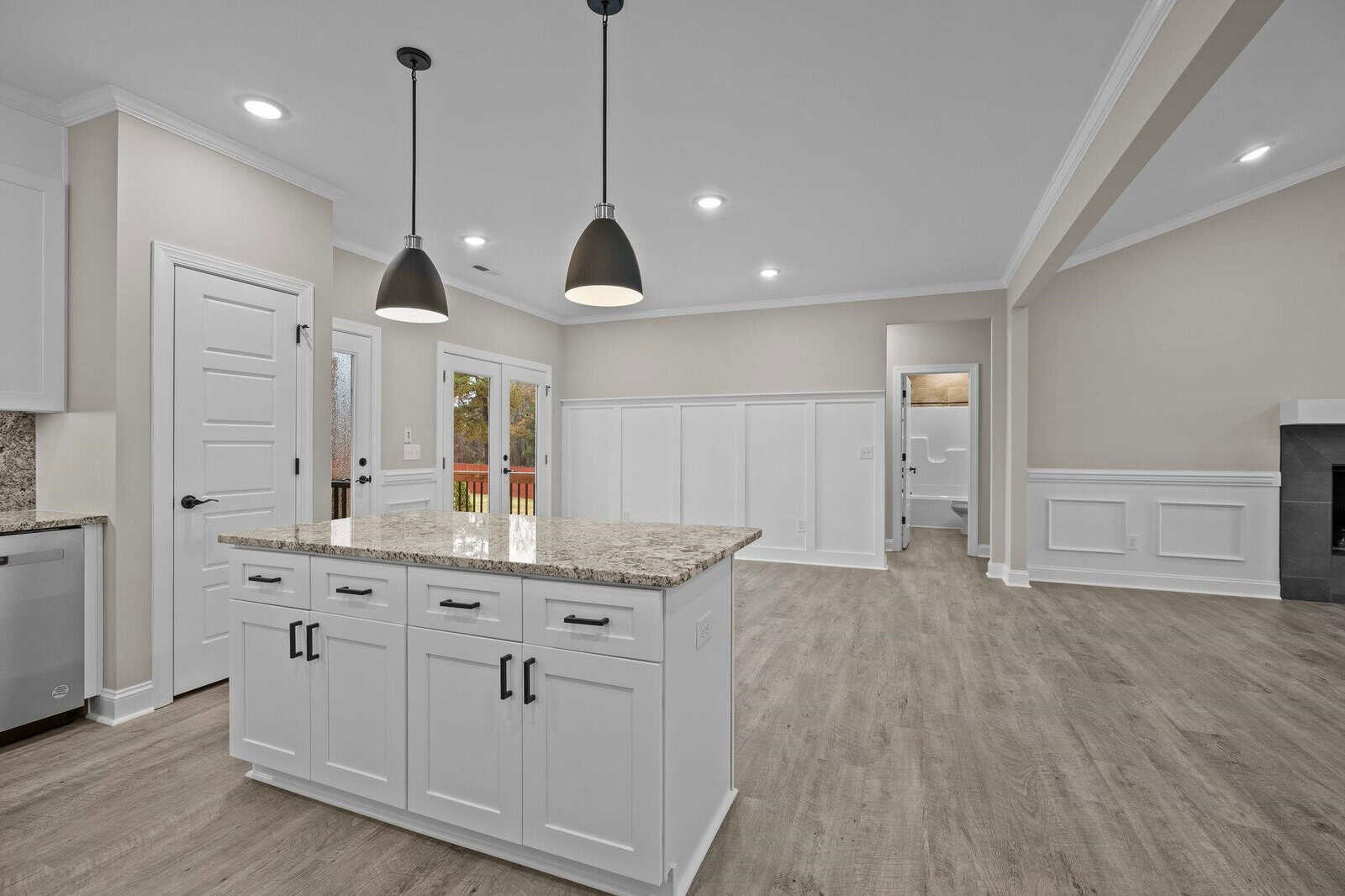 A modern kitchen with a central island, granite countertops, and pendant lighting, leading to a living area with a fireplace.