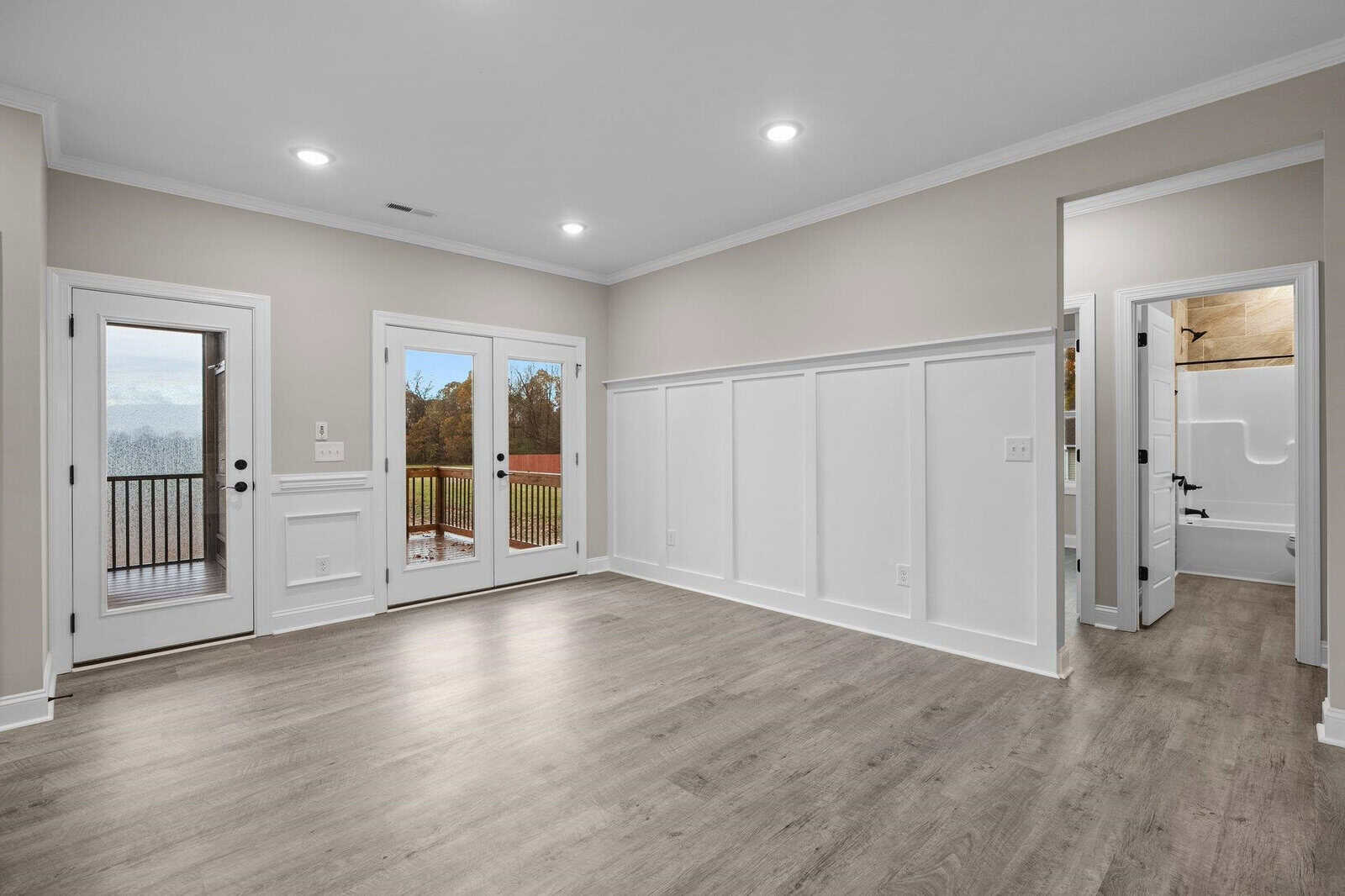 A spacious, empty room with laminate flooring, white walls, recessed lighting, and multiple doors including french doors leading to an outdoor deck.