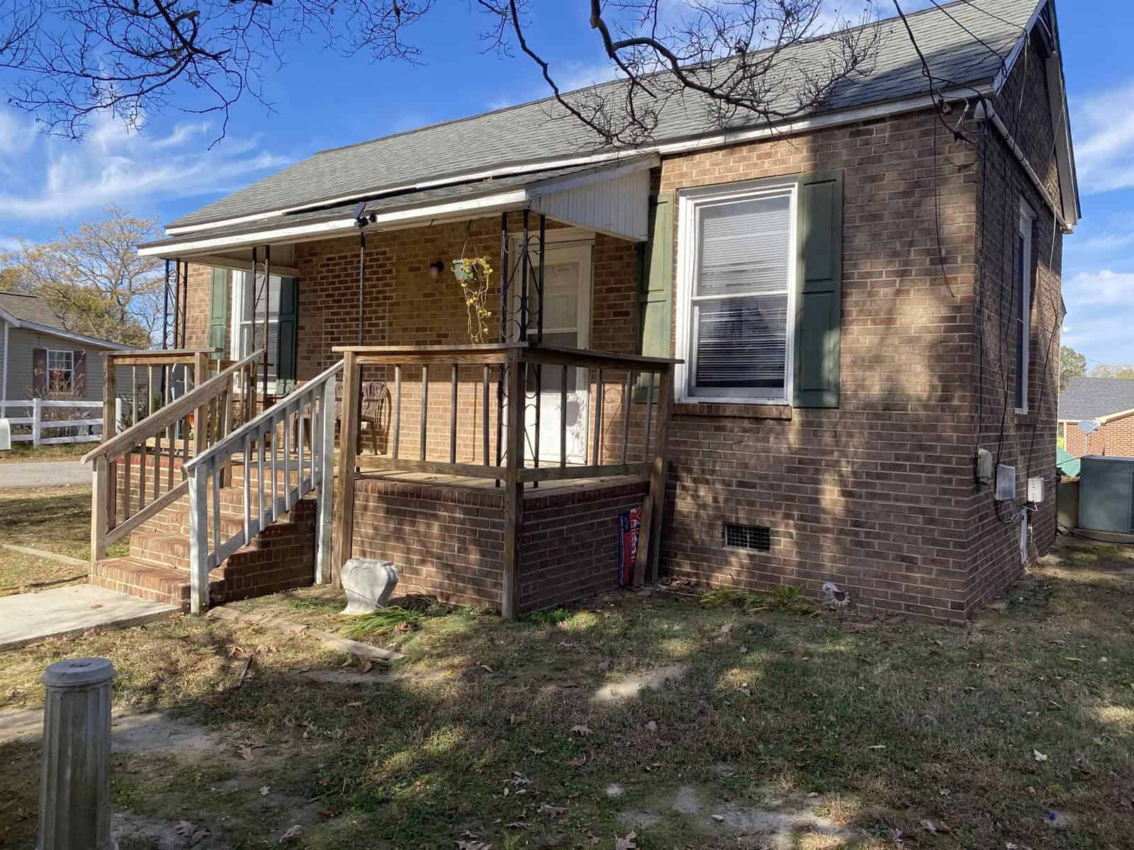 A brick suburban house with a small wooden porch and stairs on a sunny day.