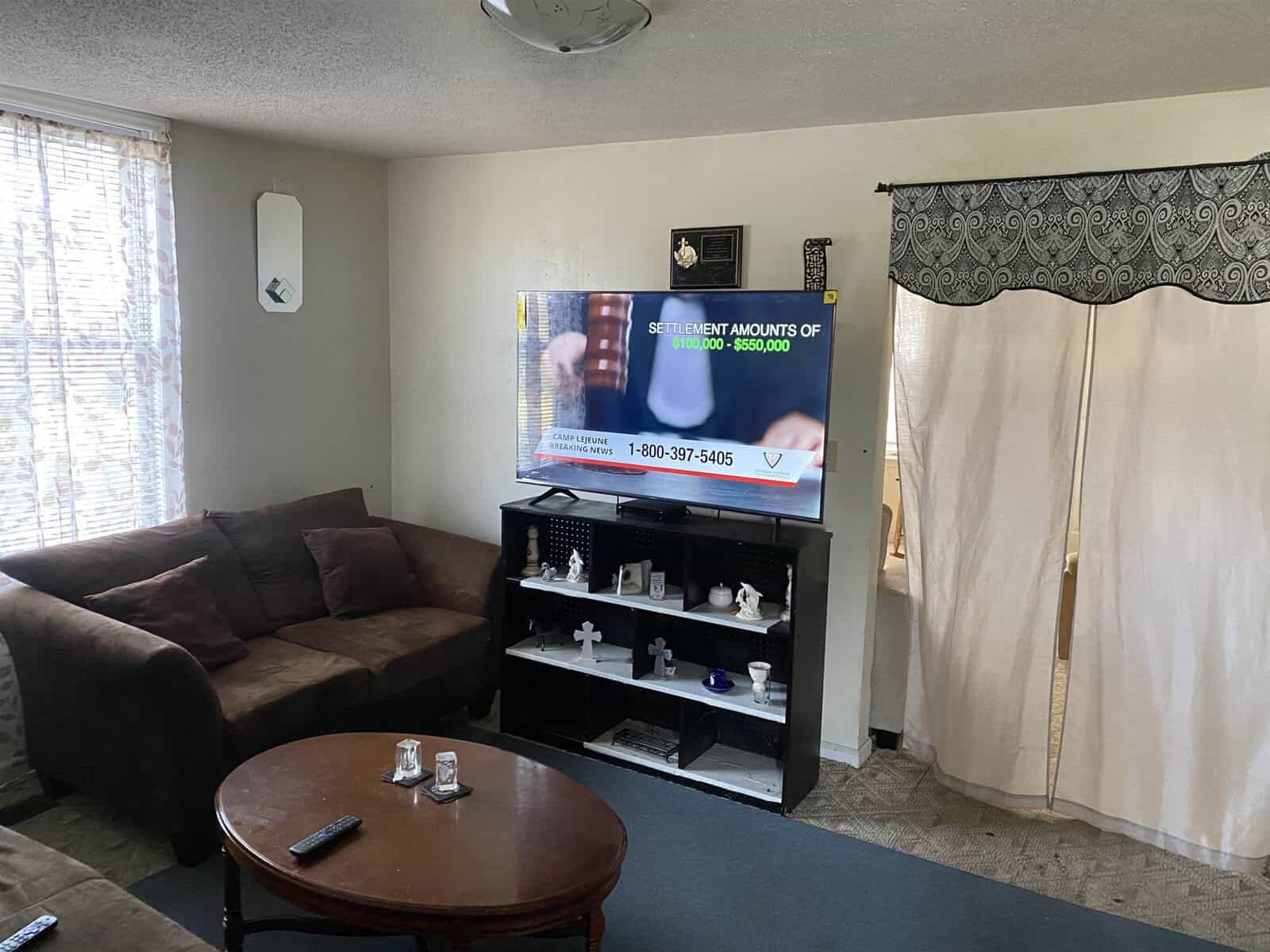 A living room with a brown sofa, wooden coffee table, and a television displaying an infomercial, with a tv stand holding various items beneath it.
